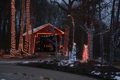 A covered bridge with Christmas lights and the trees surrounding the bridge decorated